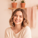 A happy Gen-Z woman smiling, embodying a soft coquette aesthetic with warm lighting and a cream and blush pink background.